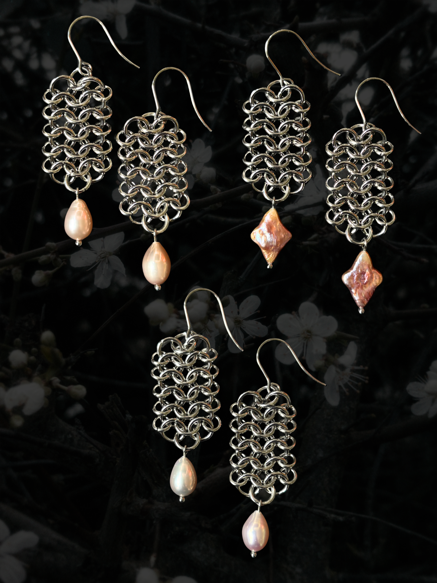 Three pairs of handmade silver-tone chainmail earrings with dangling pink freshwater pearl beads, displayed against a dark, blurred background of white blossoms.