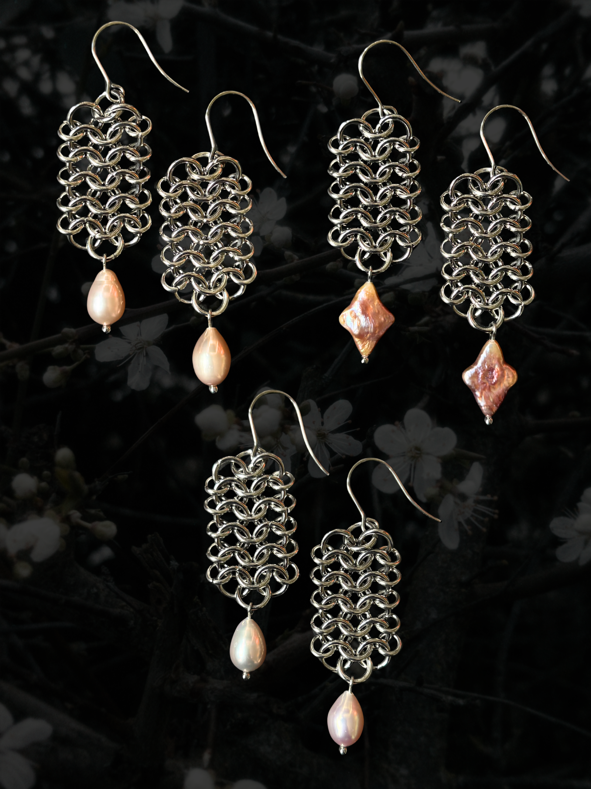 Three pairs of handmade silver-tone chainmail earrings with dangling pink freshwater pearl beads, displayed against a dark, blurred background of white blossoms.
