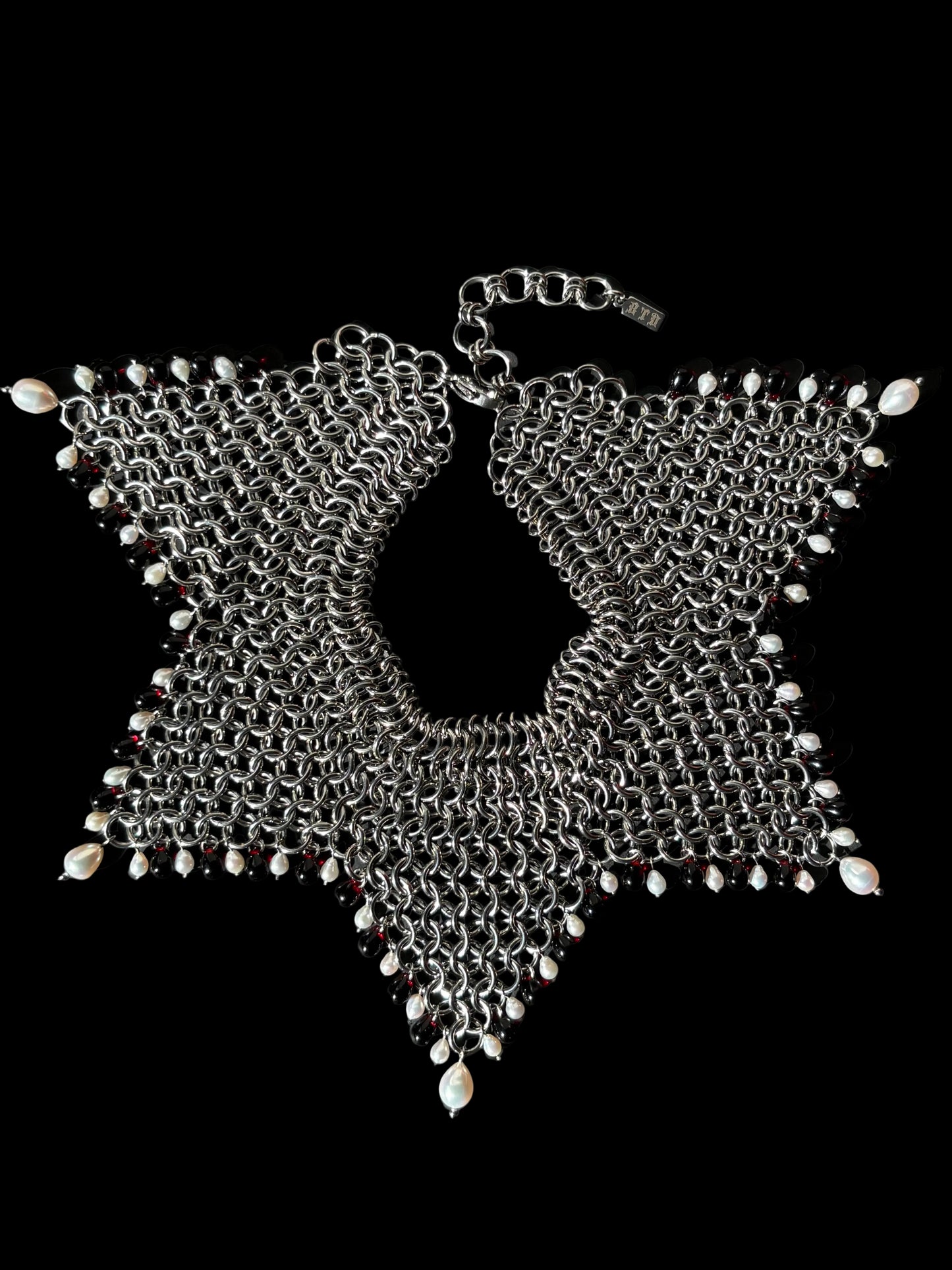 A stainless steel chainmail collar necklace with red glass beads and white teardrop pearls, laid flat on a black background.