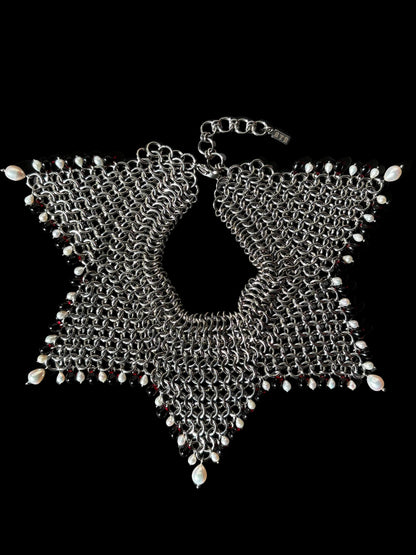 A stainless steel chainmail collar necklace with red glass beads and white teardrop pearls, laid flat on a black background.