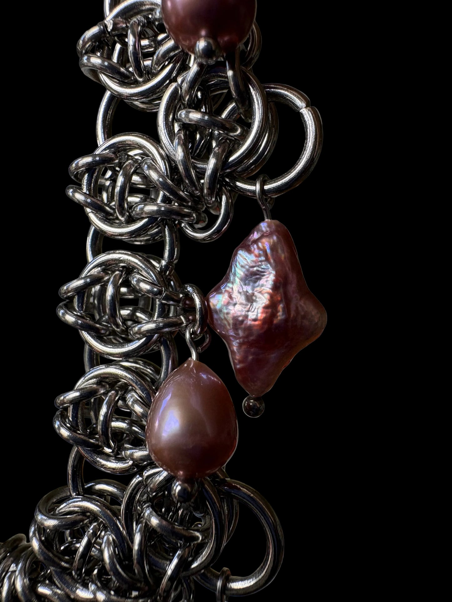 A close-up of a handmade chainmail necklace with purple teardrop and four point star pearls