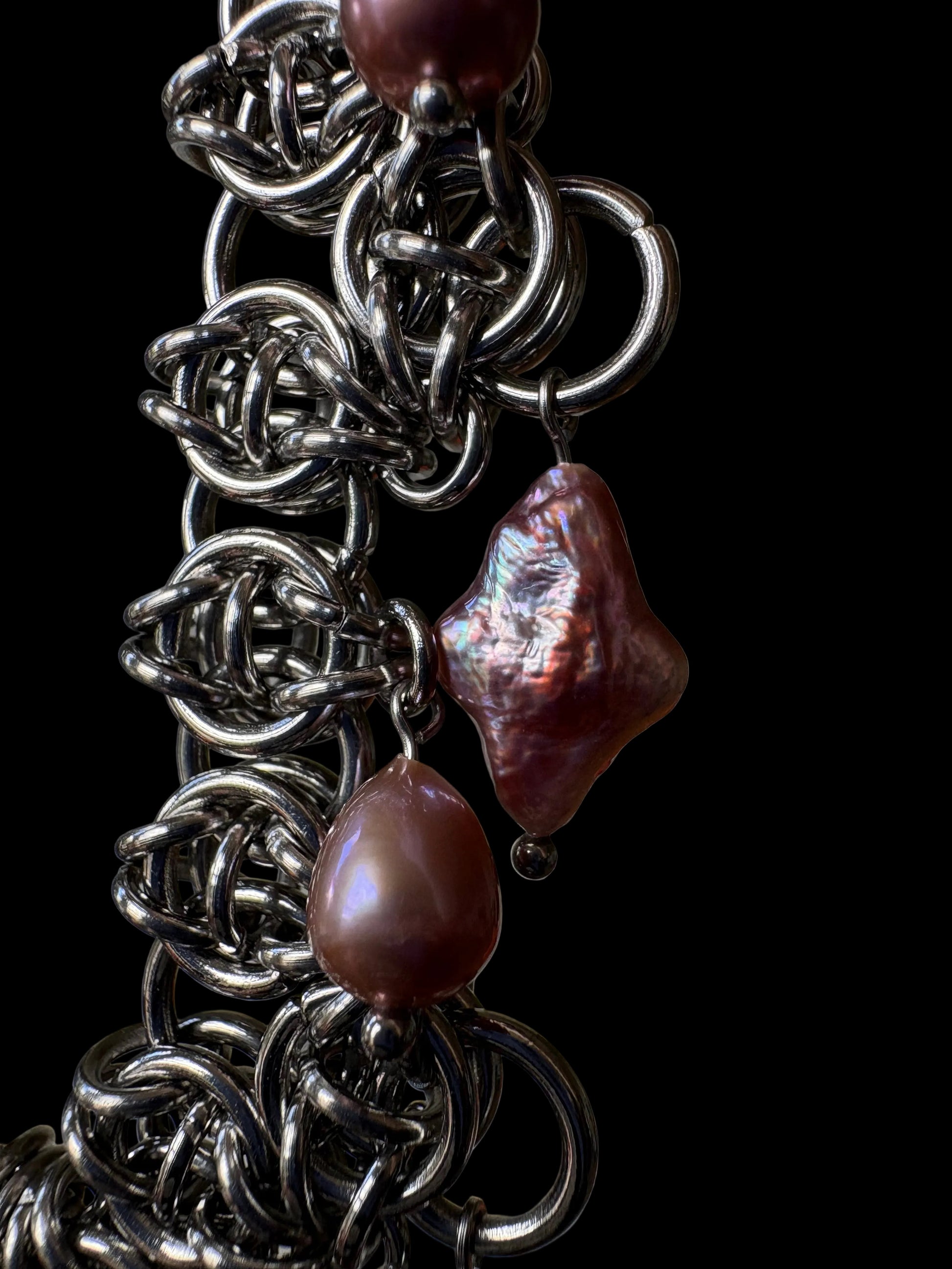 A close-up of a handmade chainmail necklace with purple teardrop and four point star pearls