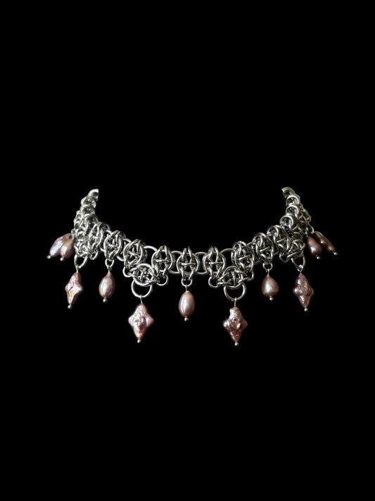 A stainless steel chainmail choker necklace with dangling purple teardrop and four point star pearls, displayed on a black background.